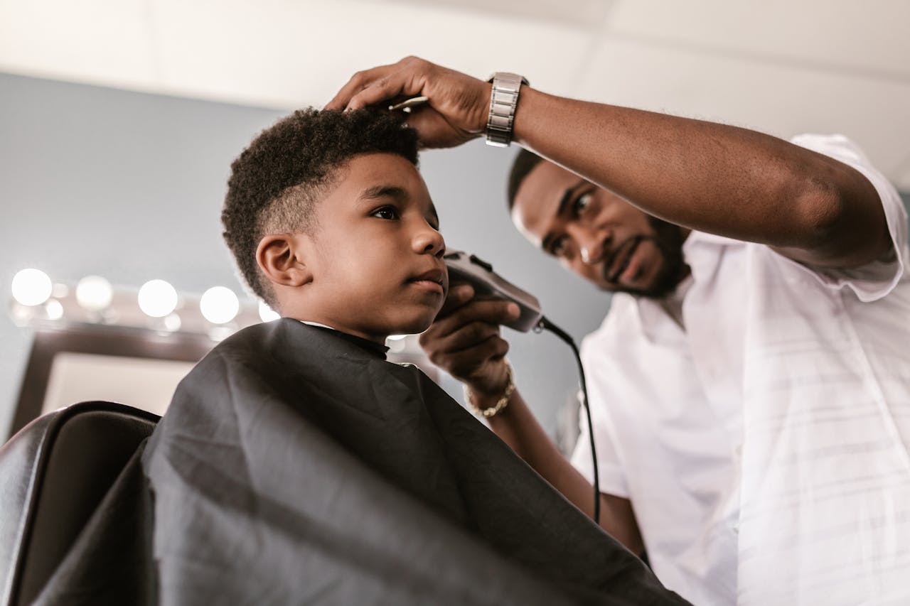 A barber skillfully trims a young boys hair using clippers. Indoor barbershop setting with focus on grooming.